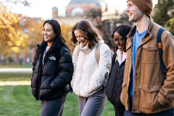 Four students walking next to each other, they are smiling as they look forward