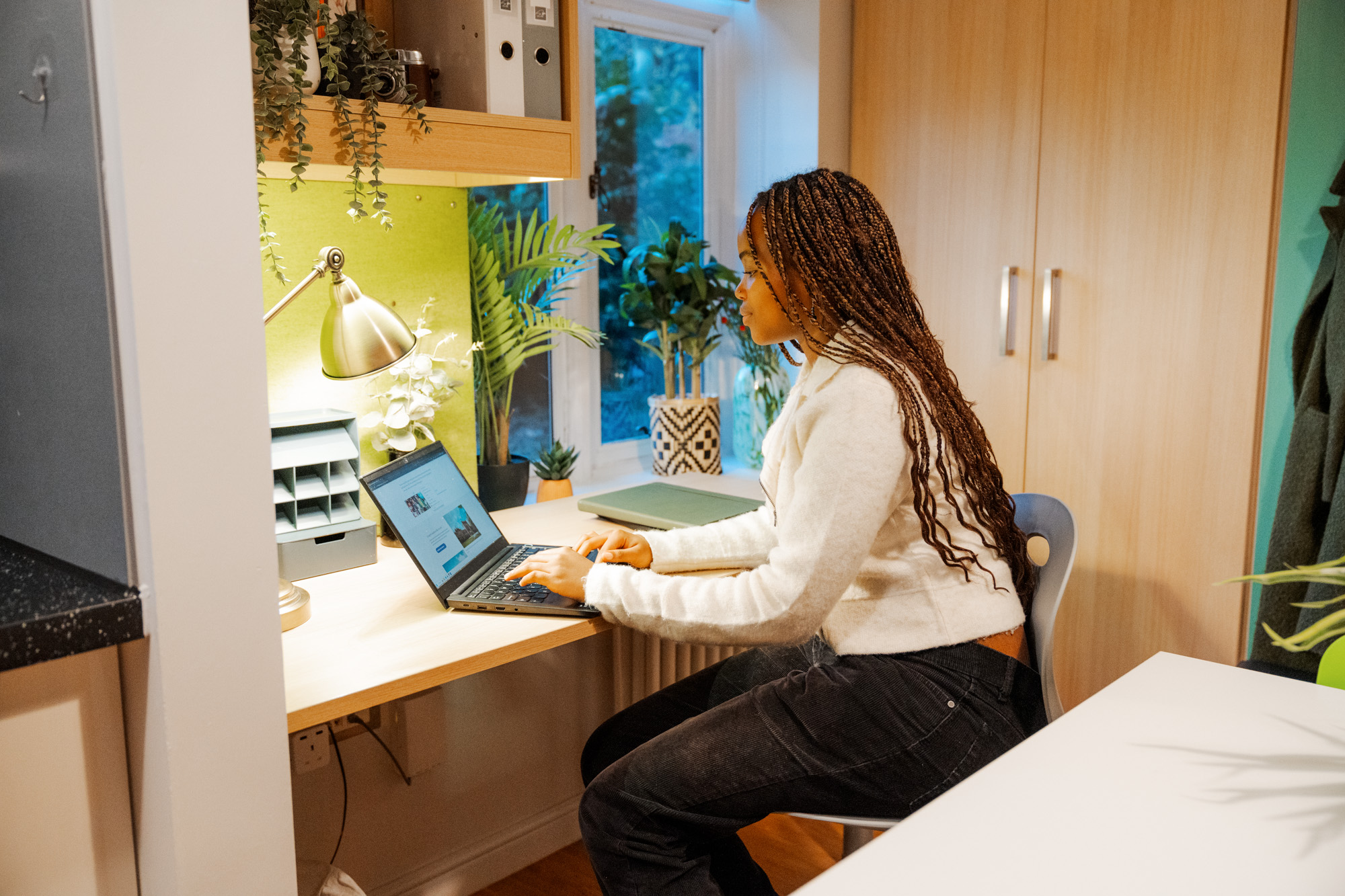 Female student on laptop in room, surrounded by green plants