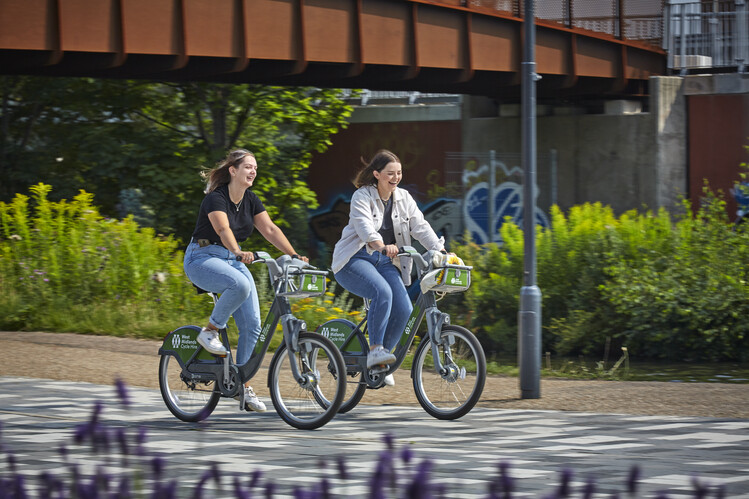 Two students riding bikes on campus while laughing.