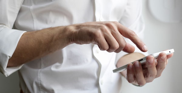 A man's hands with one holding a smartphone and the other tapping the screen