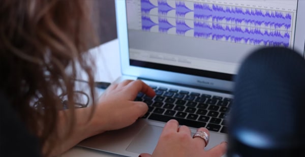 Woman doing audio editing on a laptop with sound waves on-screen