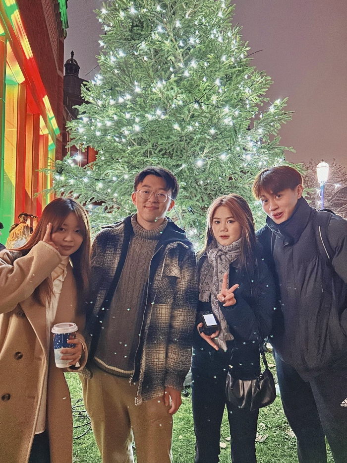 International students smiling in front of Christmas tree on campus.