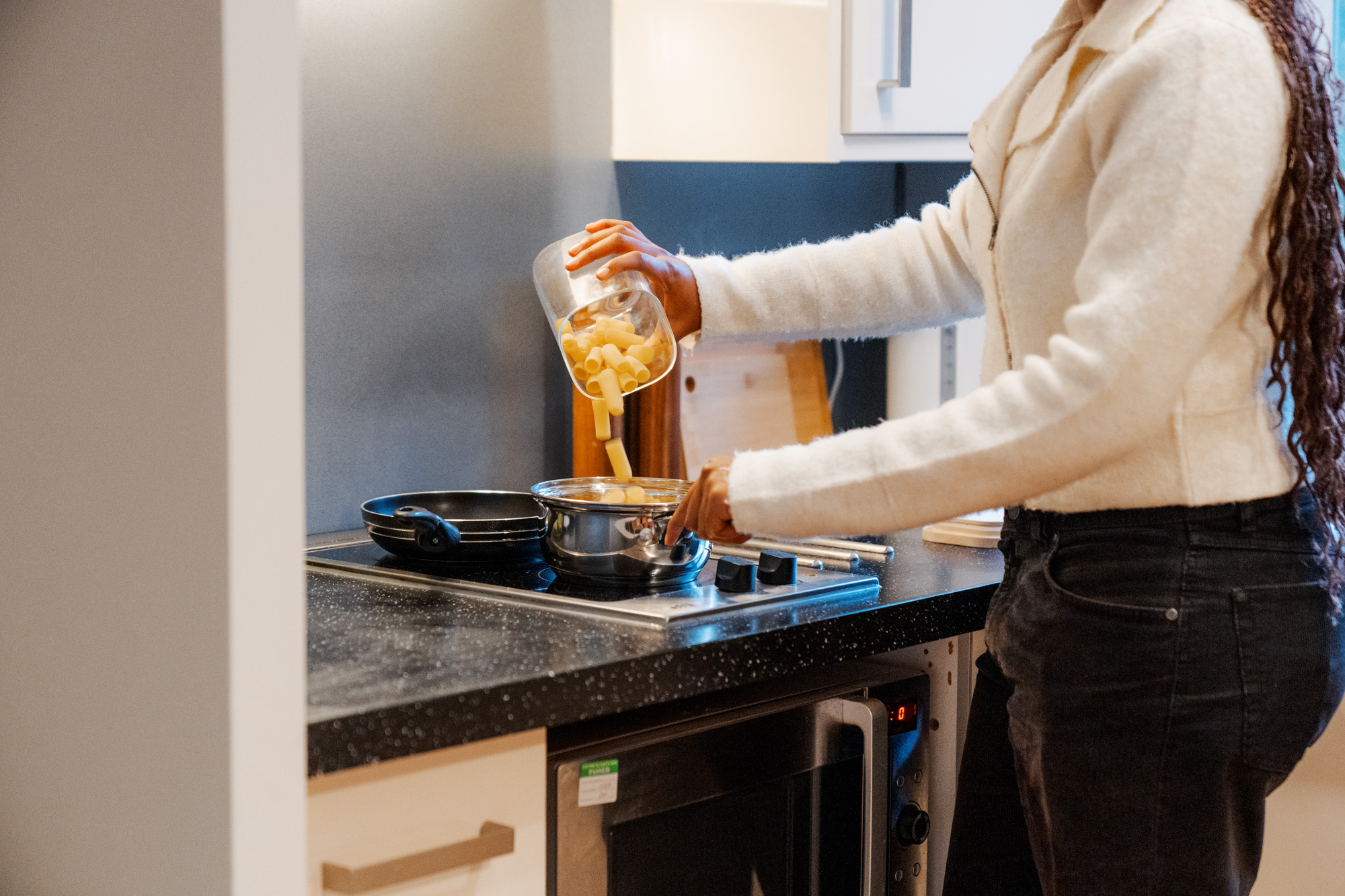 Student pouring pasta into a pan in their kitchen