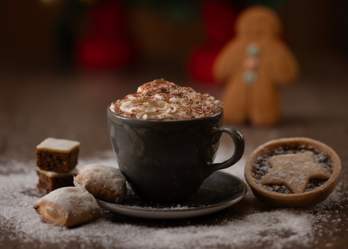 Mince pies and other festive treats, placed around a cup of hot chocolate with whipped cream.