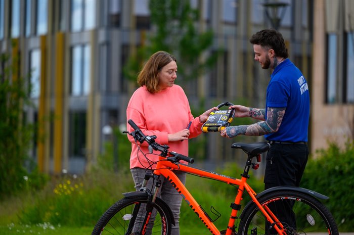 Community Safety Officer handing a D-lock to a student on campus for their bike.