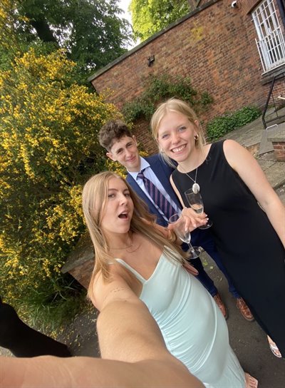 Three students smile at the camera in a selfie, dressed in formal outfits