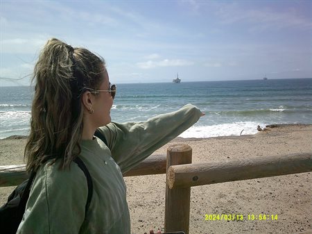 A girl points at the sea at the beach.