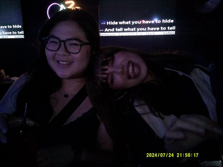 Two girls smile at the camera in a dimly lit room.