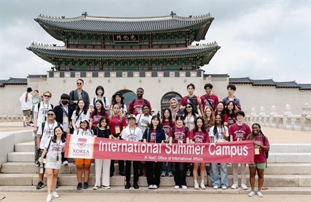 A group of students stand holding a banner on some outside steps.