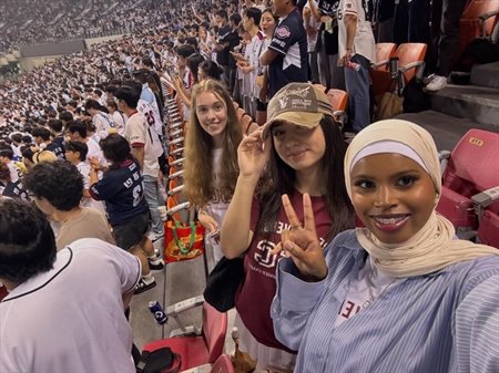 A group of friends in a stadium smile and hold up peace signs.