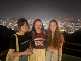 Three girls smile at the camera in front of a city skyline.