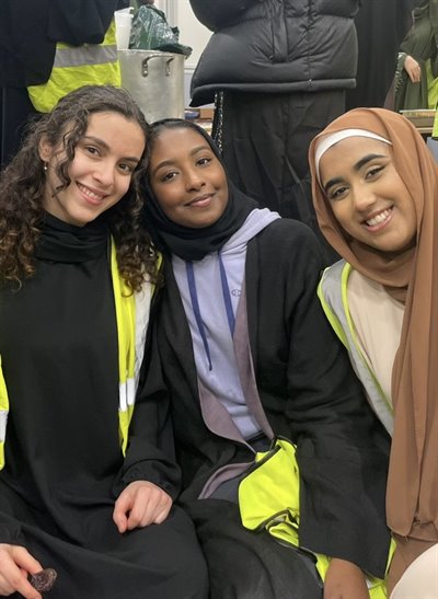 Three girls smile at the camera in high visibility jackets.