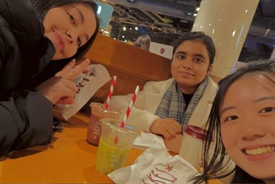 Three girls smile at the camera in a selfie as they eat takeout food