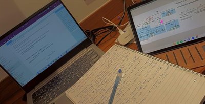 A laptop, tablet, and book full of notes on a desk