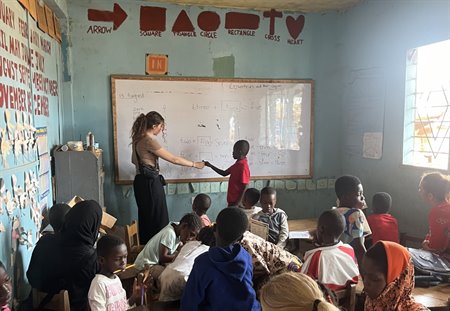 A girl teaches a lesson on a whiteboard to a class of children.