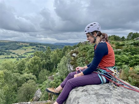 Eleanor sits on top of a rock dressed in rock climbing gear.