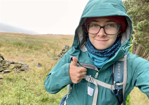 Eleanor is wearing a green rain jacket and smiling with her thumbs up.