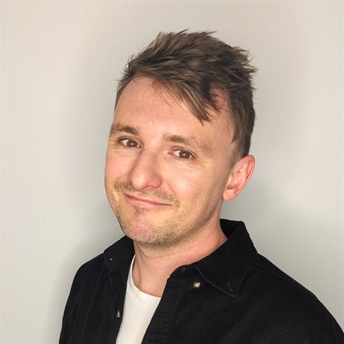 Save the Student's money expert Tom smiles at the camera, wearing a black shirt in front of a white background.